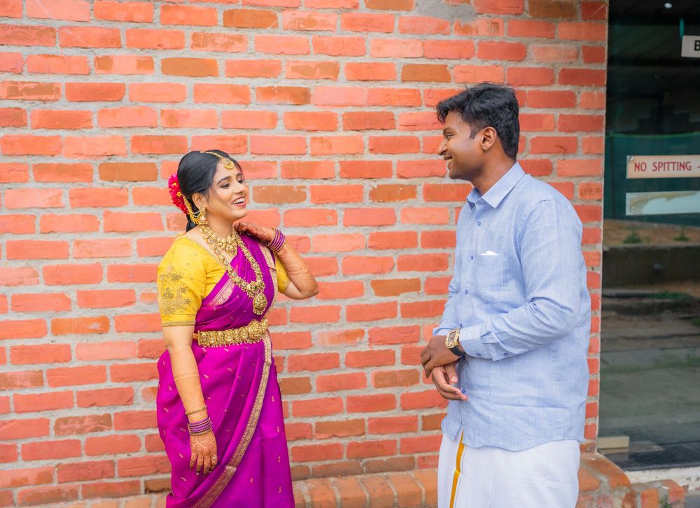 A festive interaction between two people wearing traditional Indian attire against brick wall.