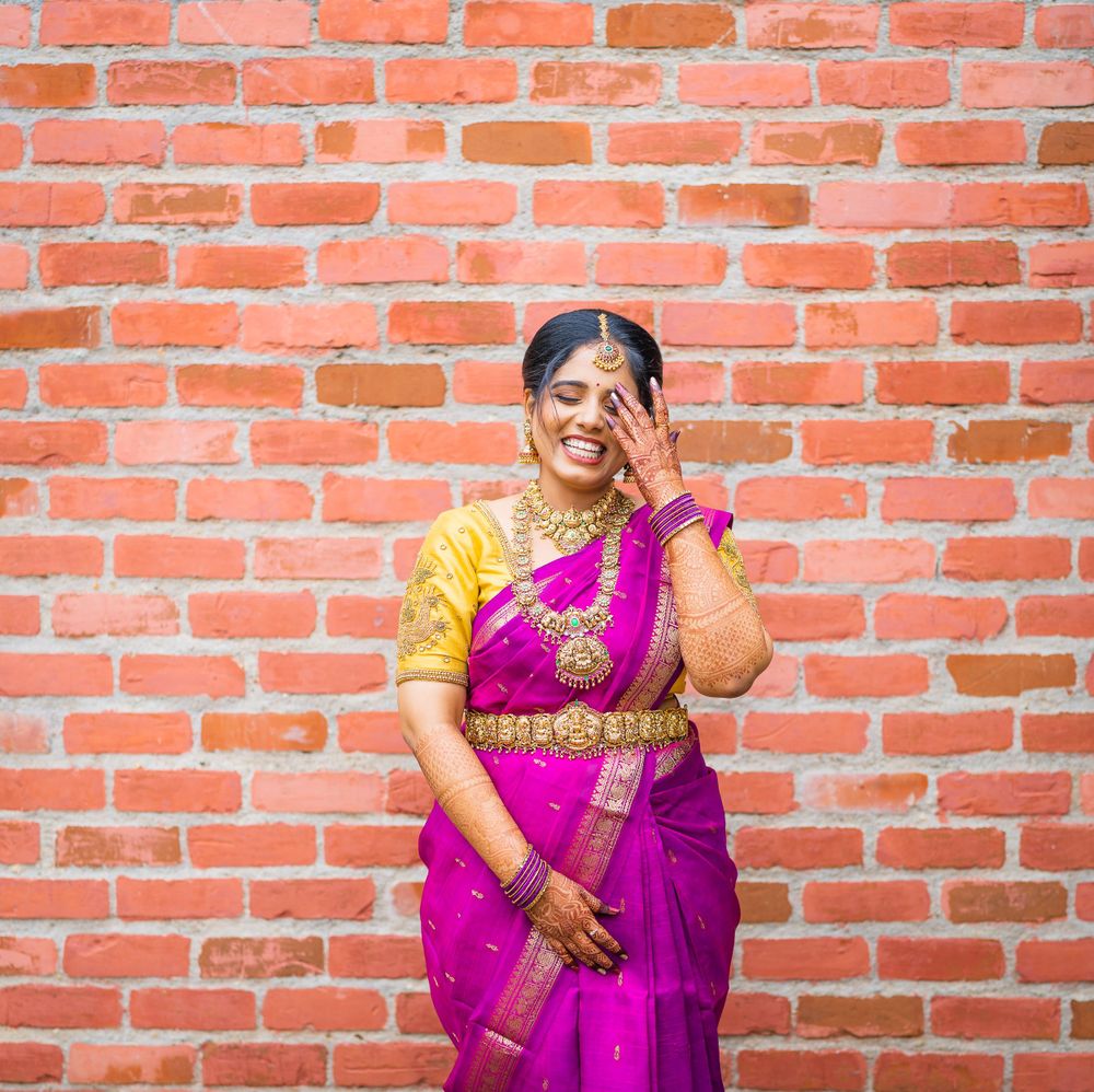 A person in a vibrant magenta and yellow sari poses elegantly against an orange brick wall.