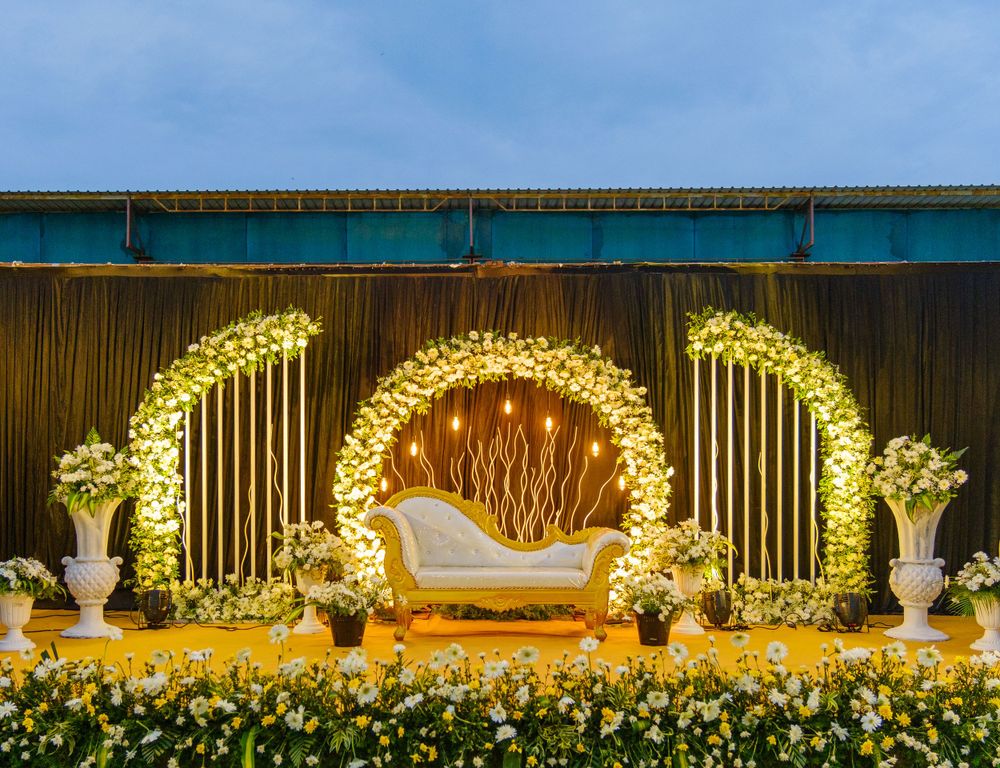 Elegant wedding stage with golden arches and white floral decorations against a blue backdrop.