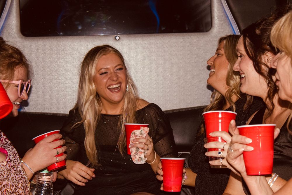 Group of women laughing and holding red Solo cups inside a party bus at night.