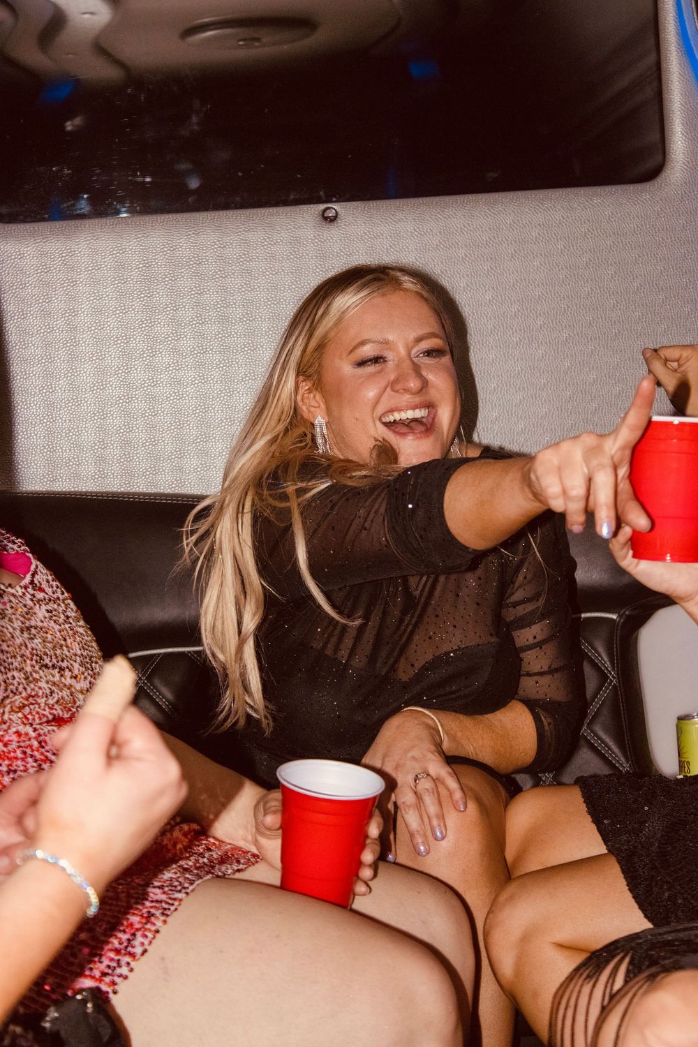 Blonde woman in black dress laughing and holding a red Solo cup inside a party limo.