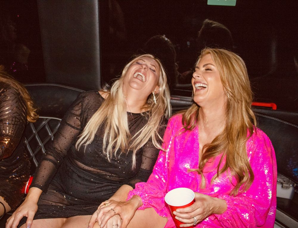 Two women laughing joyfully together at a nighttime party event.