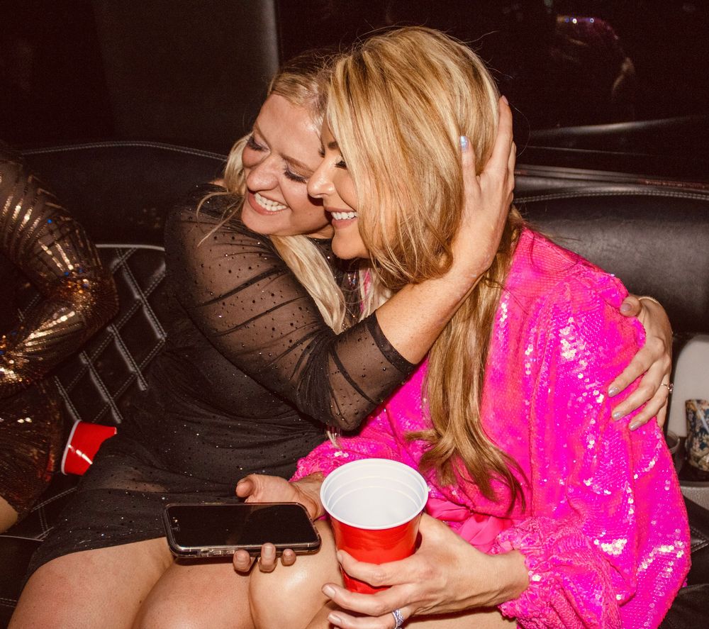Two women hugging and smiling inside a party bus during a night out.