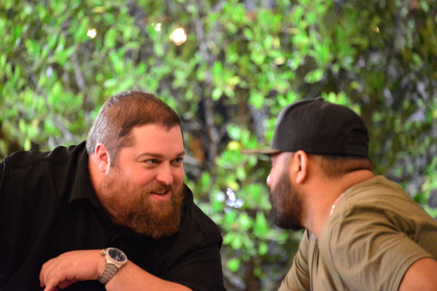 Group of friends sitting outdoors having drinks and conversation in a garden setting.
