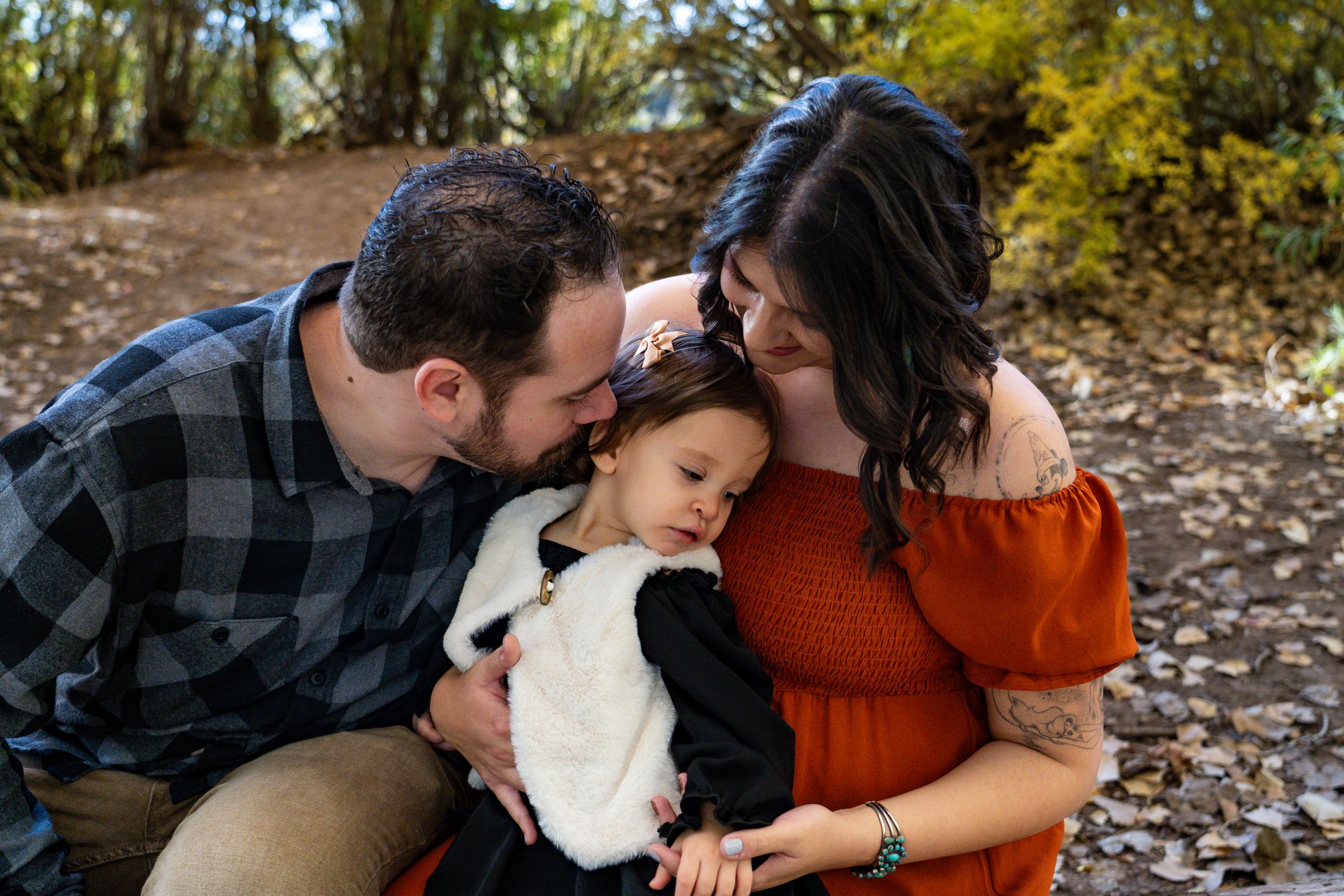 Family of three sharing intimate moment together on fallen autumn leaves.