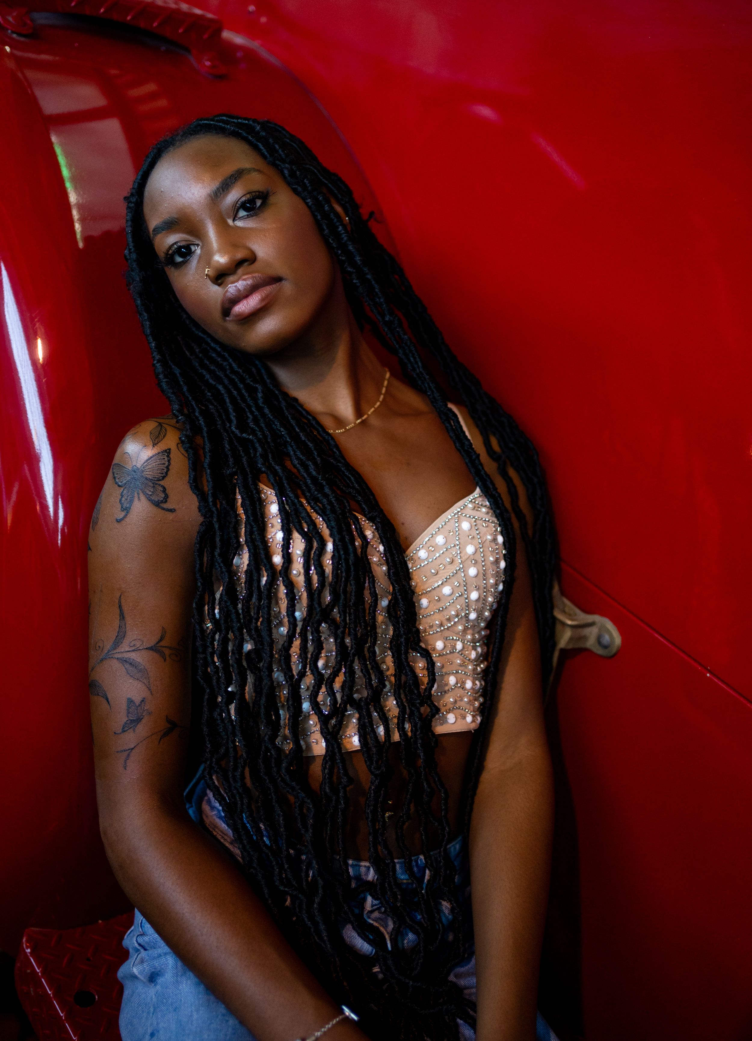 Fashion portrait against red car background with dramatic lighting.