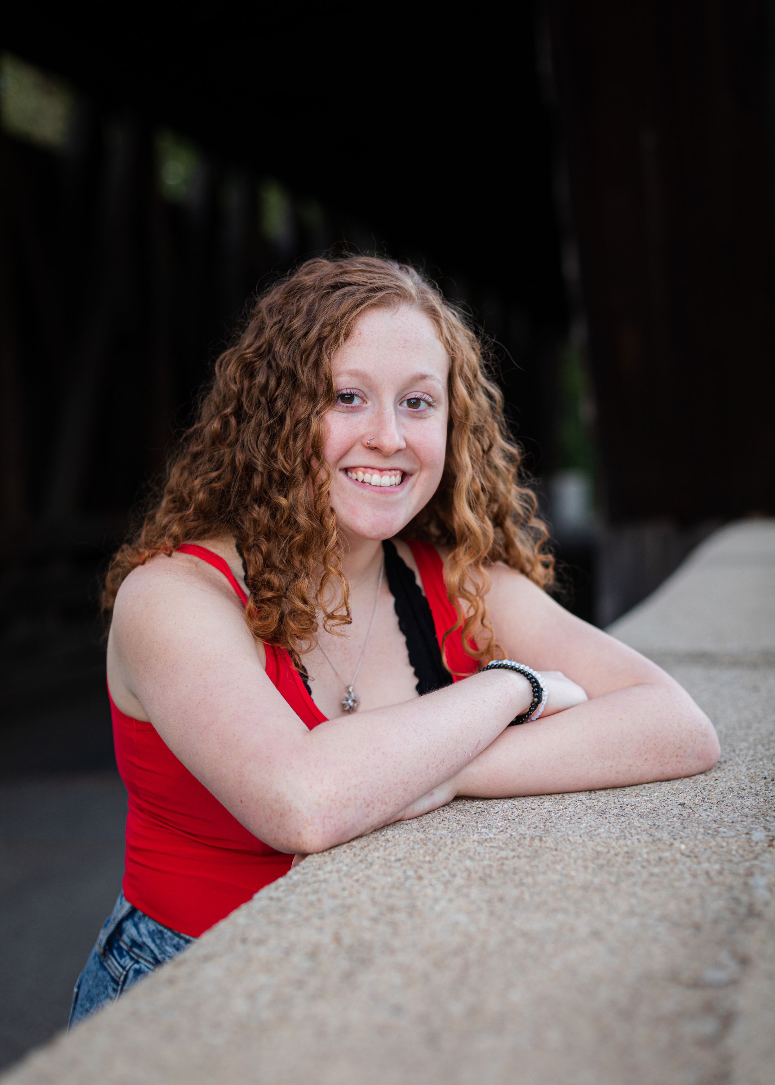 Relaxed portrait leaning on concrete surface wearing red sleeveless top.