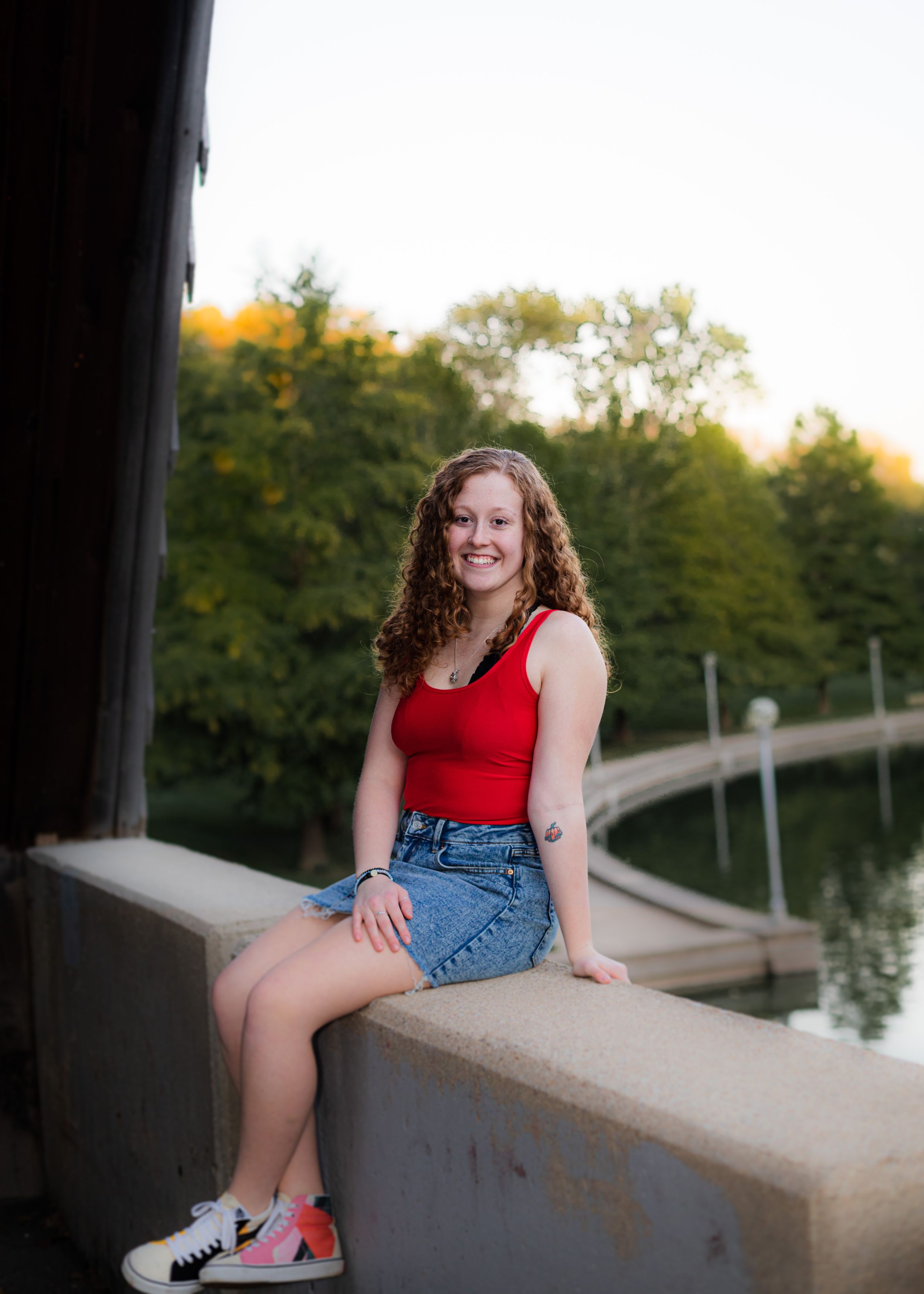 Casual outdoor portrait sitting on concrete wall wearing red top and denim shorts.