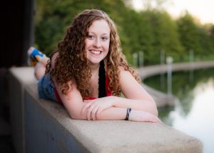 Person with curly hair resting on concrete ledge near water during sunset.