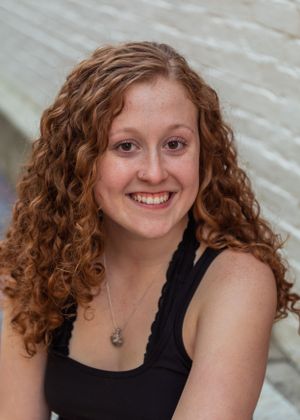 Person with curly hair wearing a black tank top smiling at the camera in a headshot series.