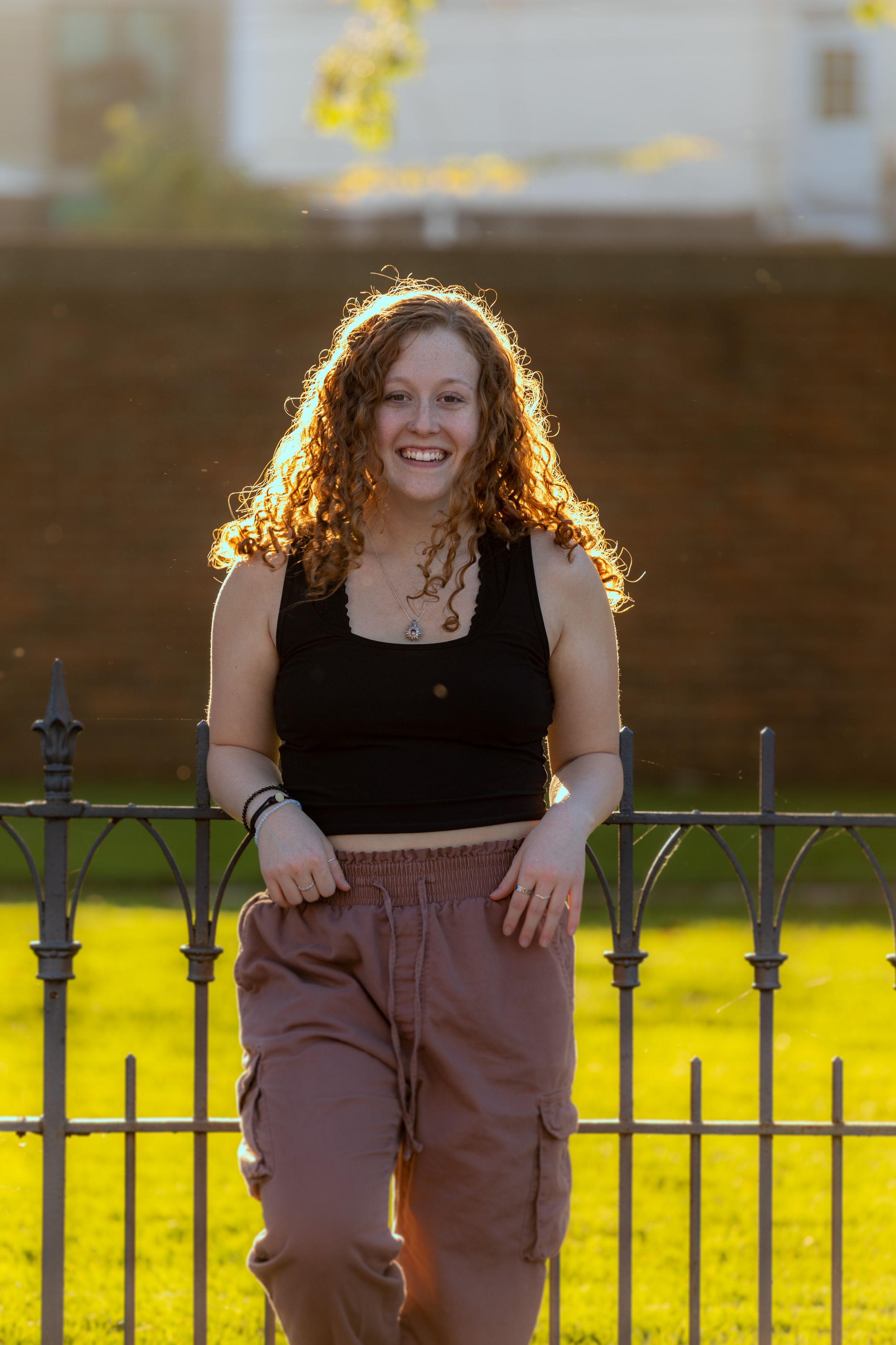 Backlit portrait by iron fence during golden hour wearing casual attire.