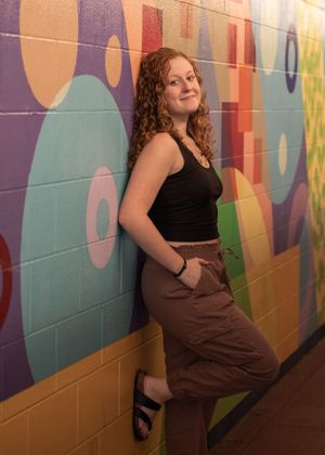Portrait against colorful geometric wall mural wearing brown and black outfit.