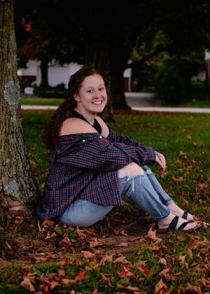 A person in a plaid shirt relaxing on autumn leaves under trees.