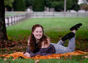 Someone lying on an orange blanket outdoors surrounded by fallen leaves.