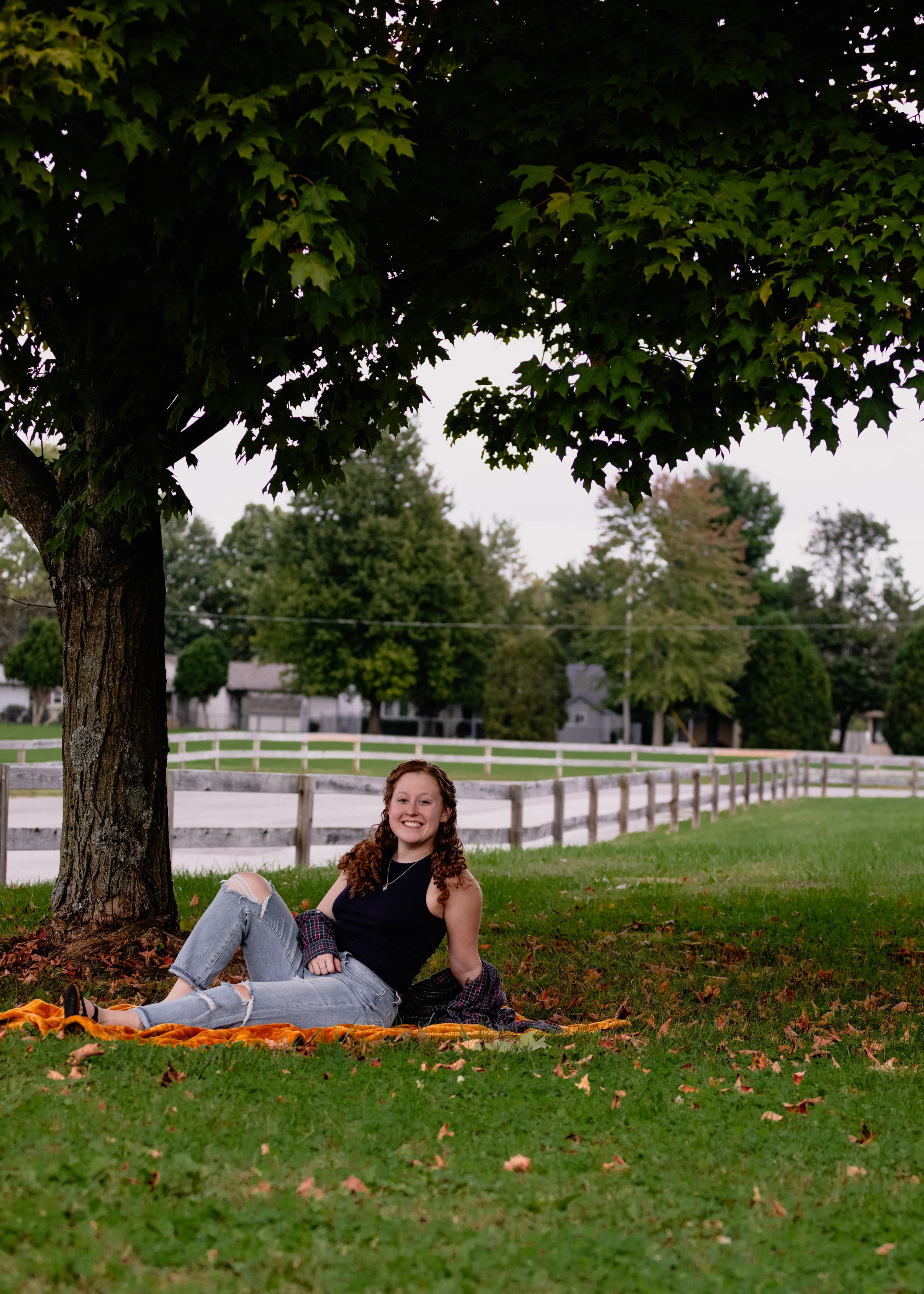 Person lying on grass near white fence on autumn day with fallen leaves.