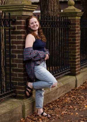 Person in plaid shirt posing casually by brick wall with iron fence during fall.