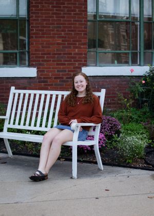 Person in burgundy sweater lounging on white bench against brick building.
