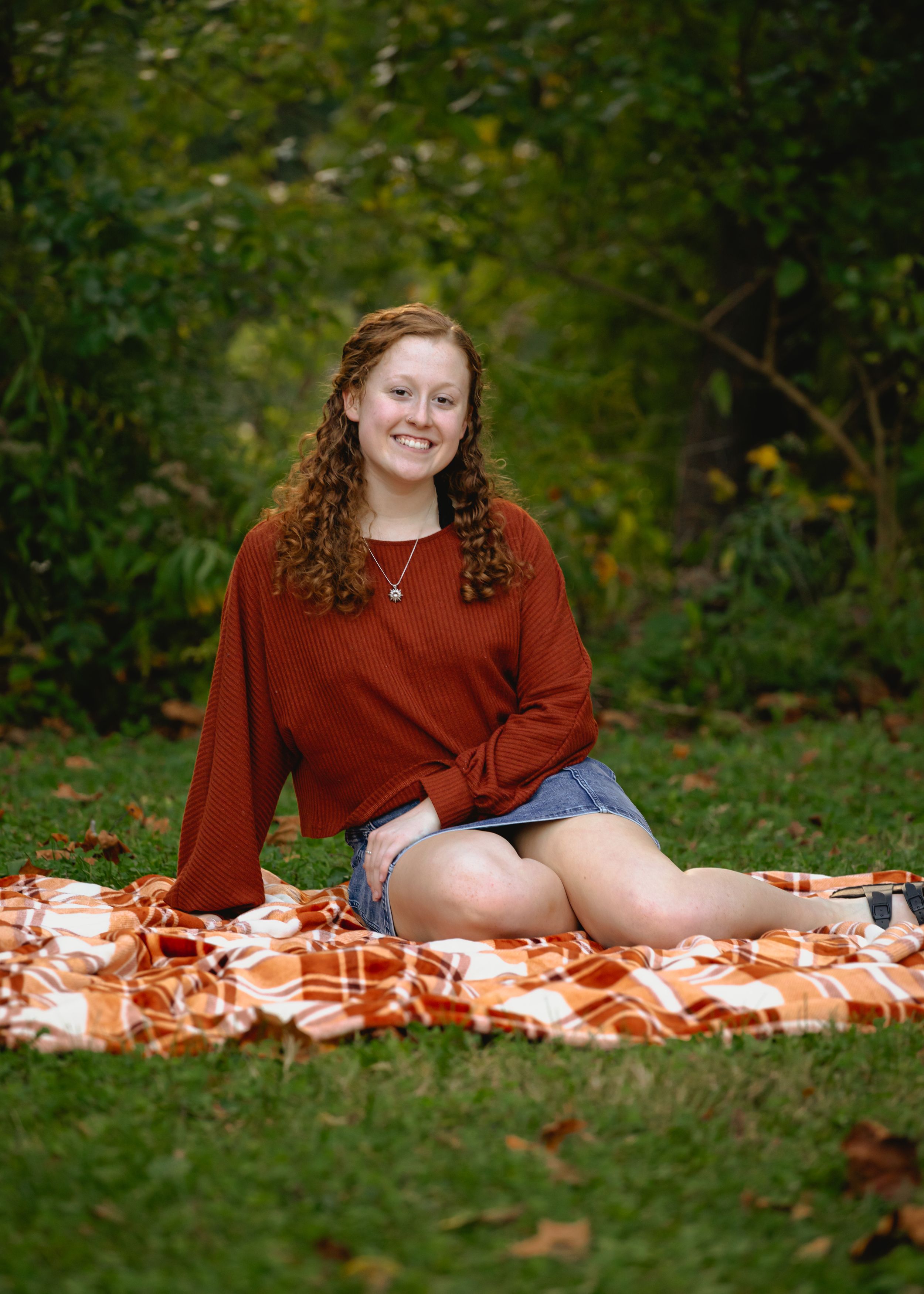 Someone posing on a patterned blanket in a park setting with green foliage.