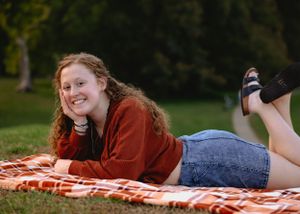 Person in casual attire relaxing on orange blanket in park setting.