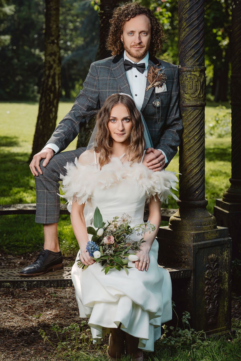 Wedding couple sits on garden bench surrounded by lush greenery.