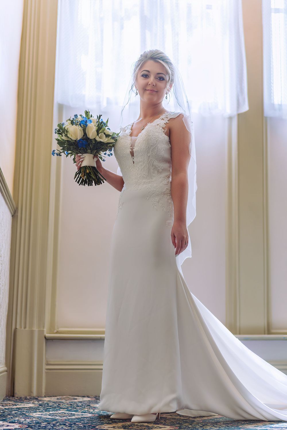 Elegant bridal portrait in sunlit room with flowing white gown.