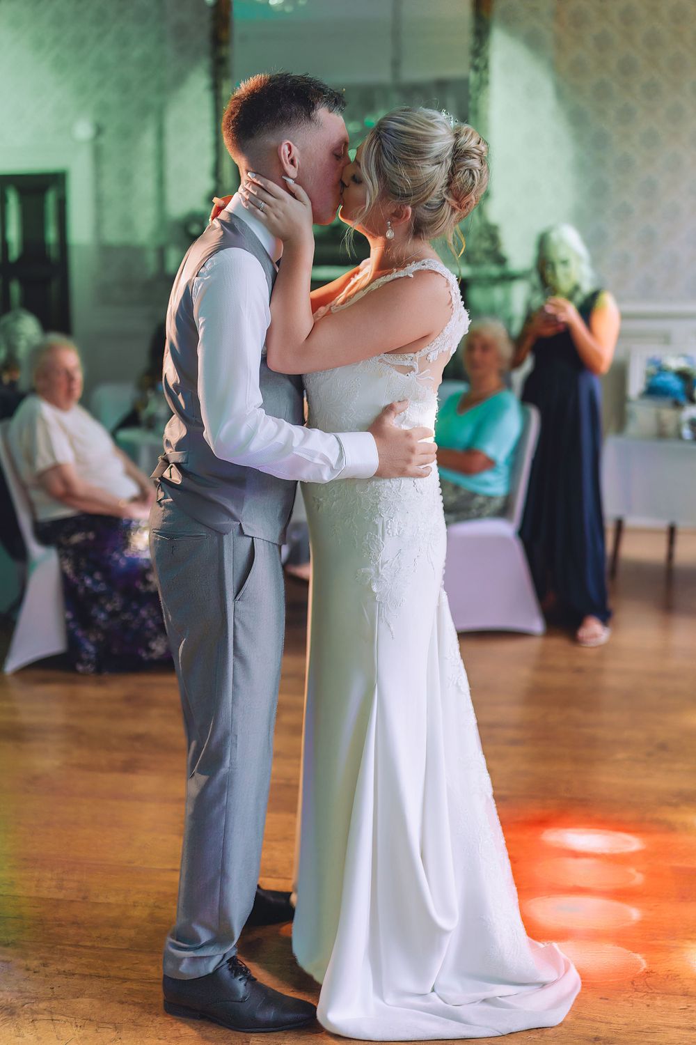 Couples slow dance on illuminated dance floor at wedding reception.