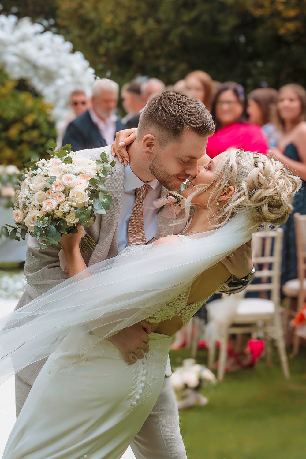 A romantic dip kiss sequence between newlyweds in a garden wedding setting with white floral bouquet and flowing veil.