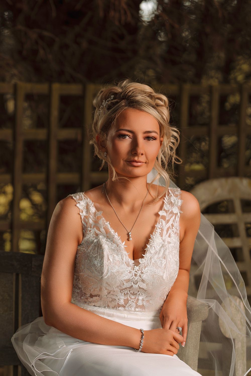 A bride in a white lace wedding dress poses outdoors against a natural wooded backdrop during golden hour.
