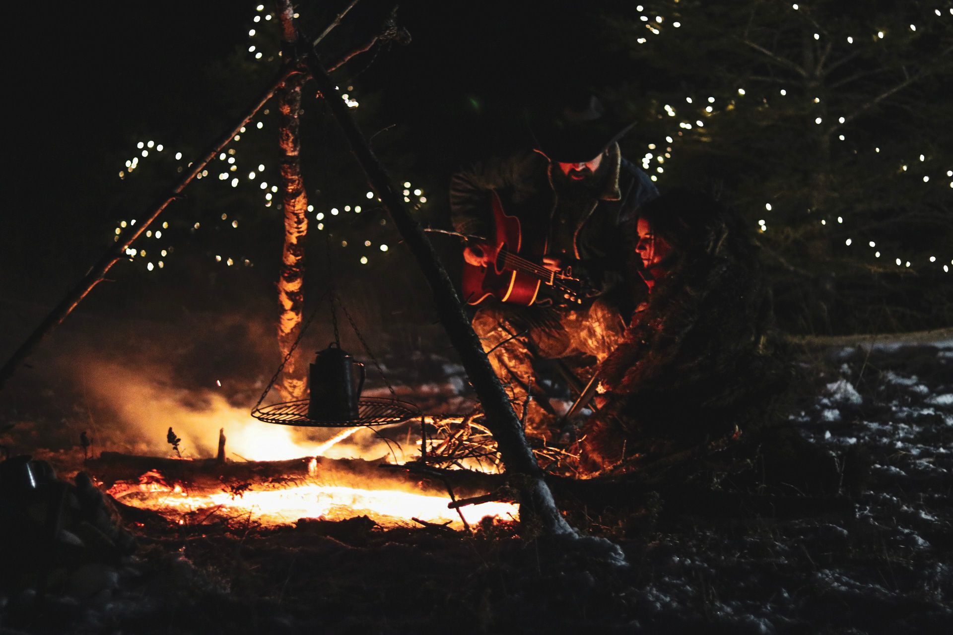 Campfire burning brightly at night with string lights visible in background.