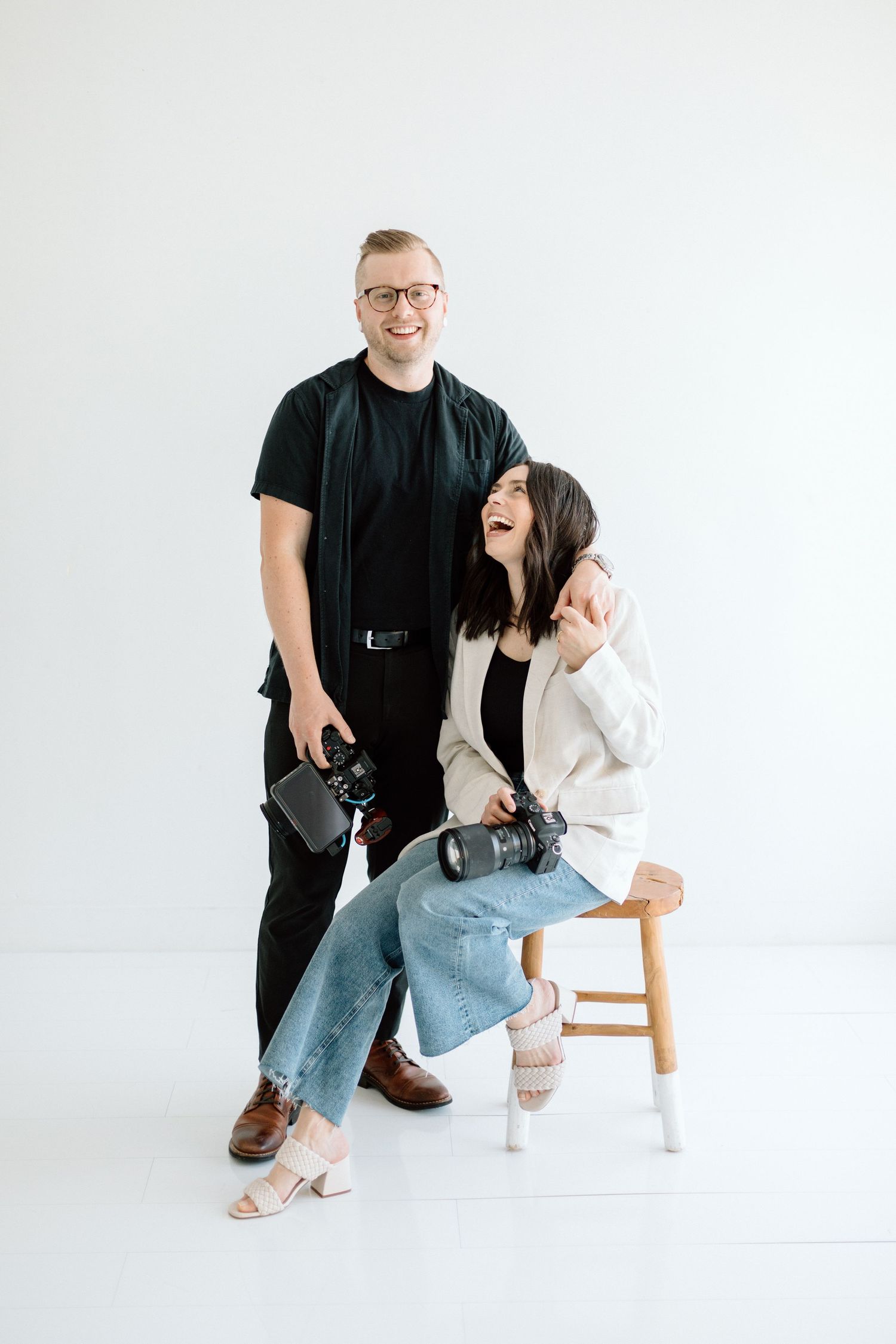 Casual studio portrait with photography equipment against white background.