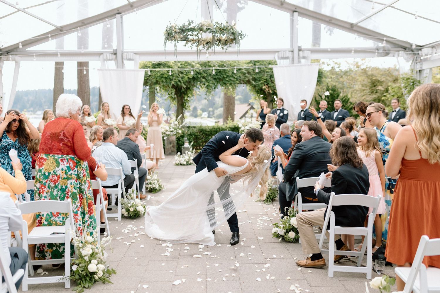 Romantic wedding kiss under a floral archway with lanterns and white flowers.