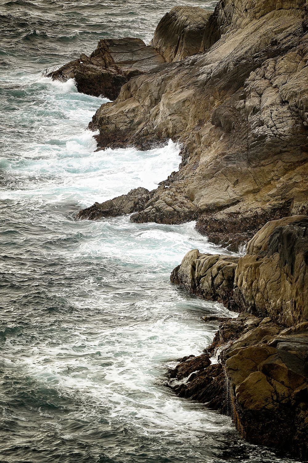Rugged coastal cliffs with waves crashing against rocky shoreline in rough seas.