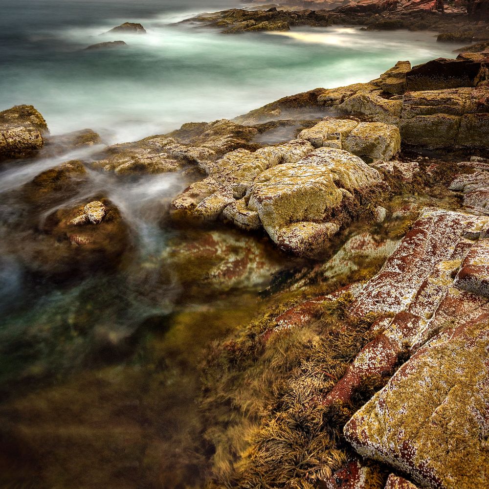 Long exposure of waves flowing over weathered coastal rocks in ethereal green waters.