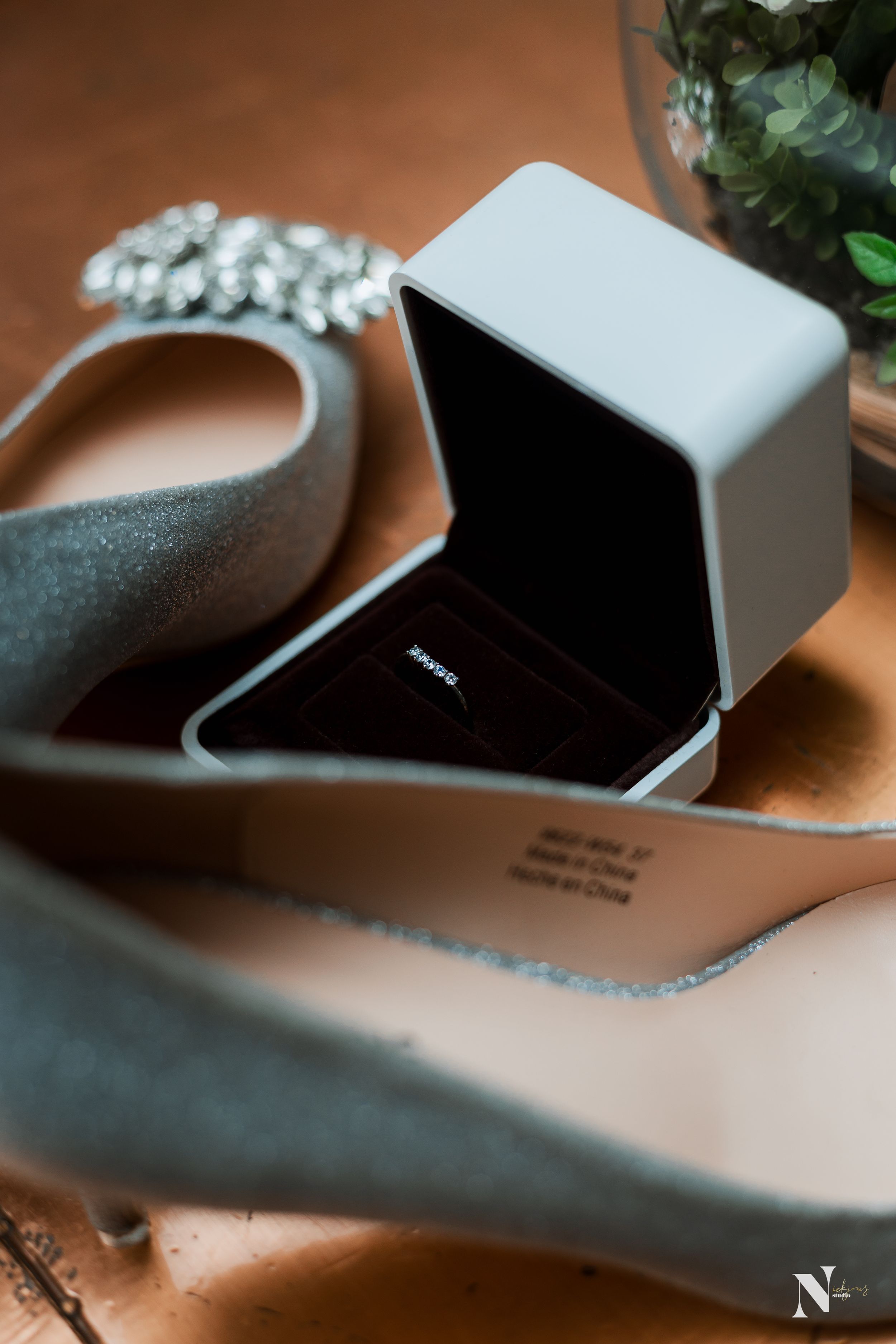 Wedding ring box and embellished bridal shoe on wooden surface with shallow depth of field.