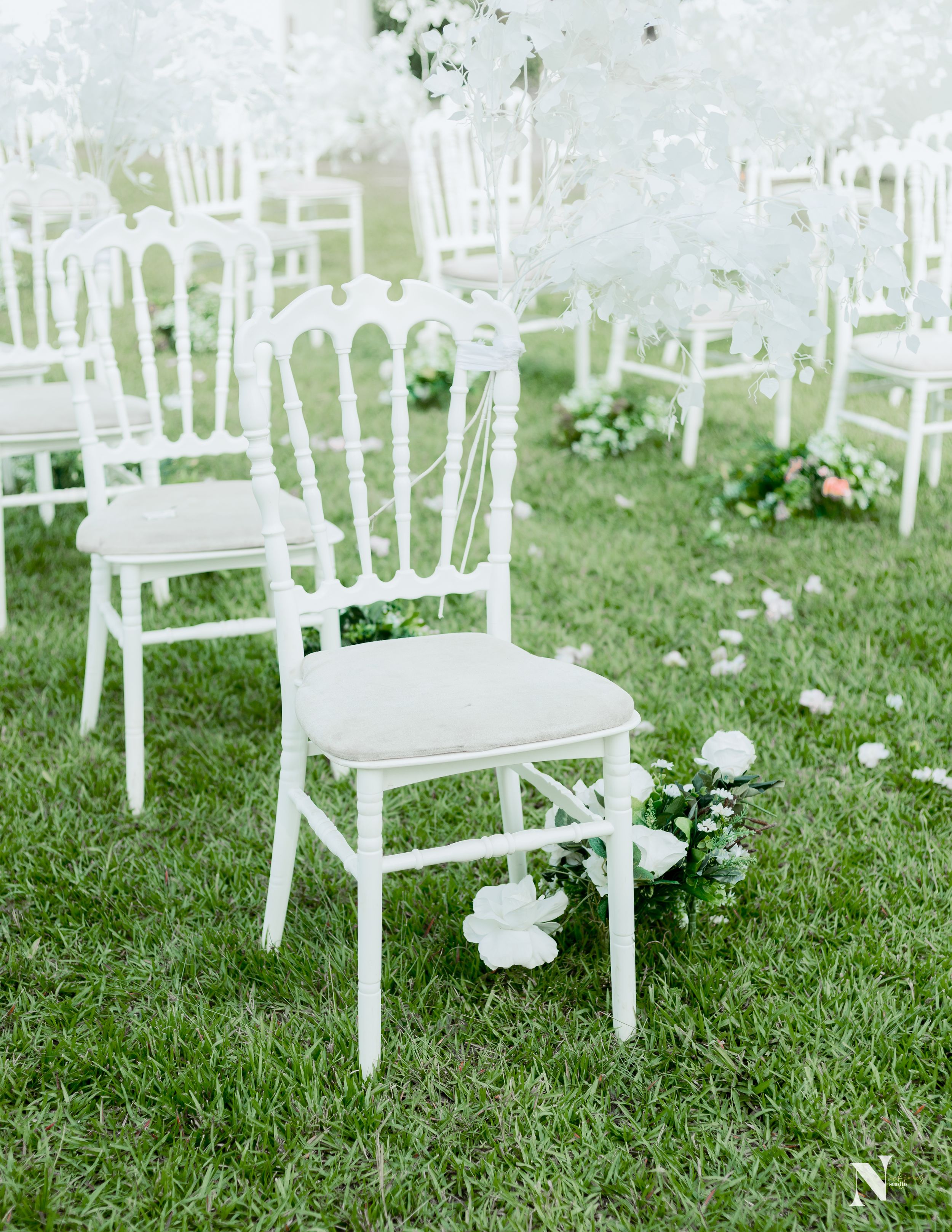 White vintage-style chairs arranged on grass for an outdoor wedding ceremony.