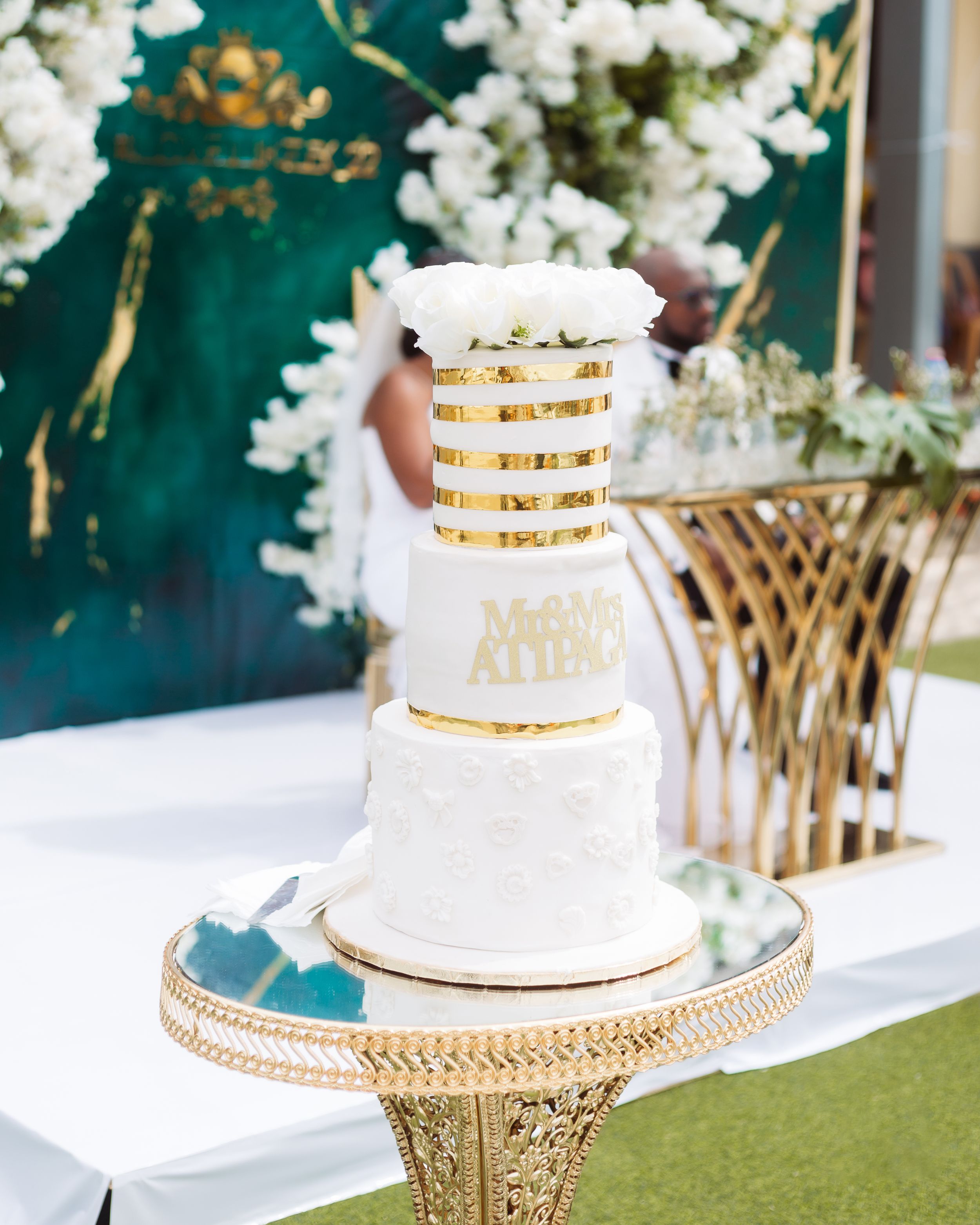 Elegant white and gold tiered wedding cake displayed on ornate gold stand.