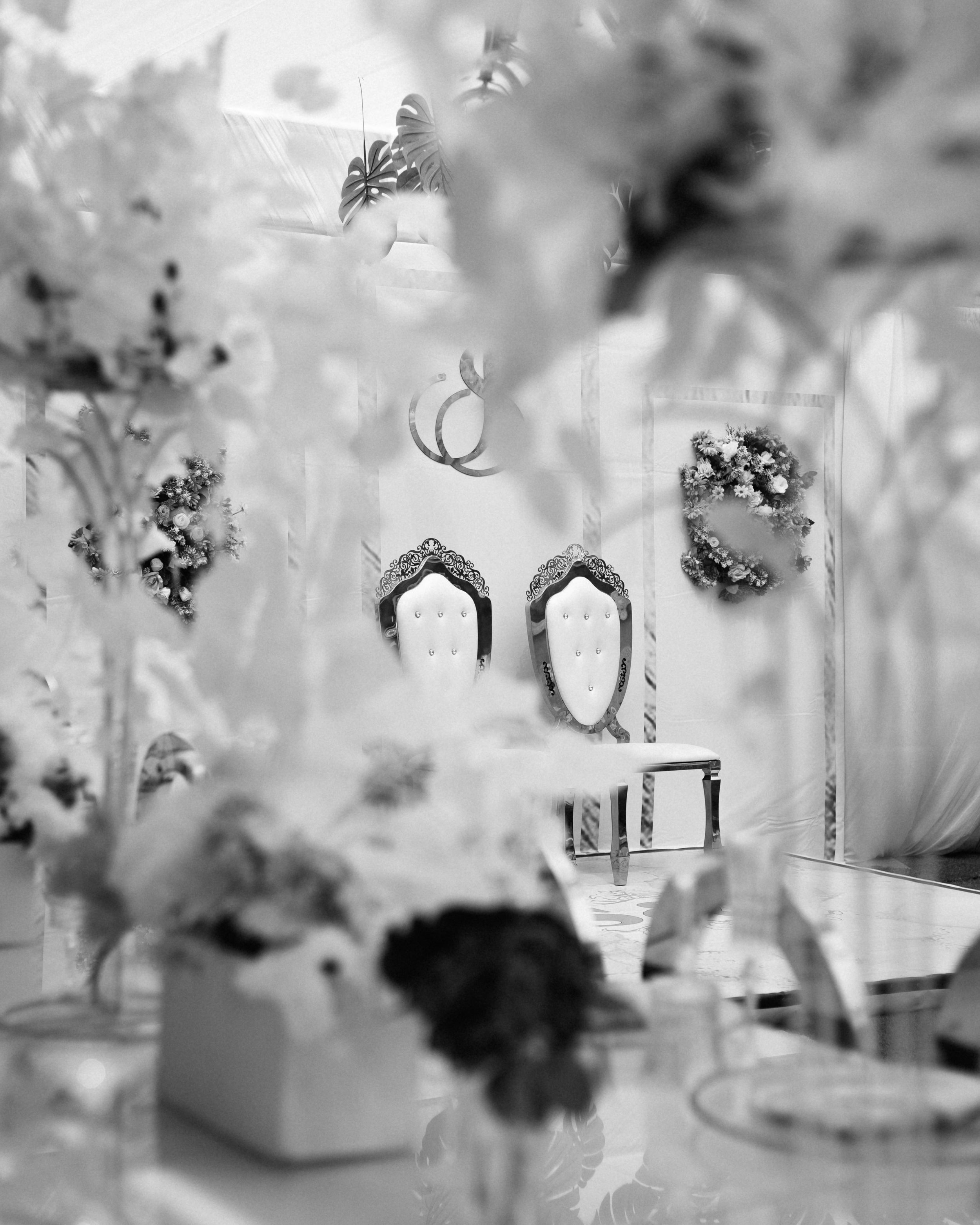 Black and white photograph of wedding table decorations with floral arrangements and decorative elements in soft focus.
