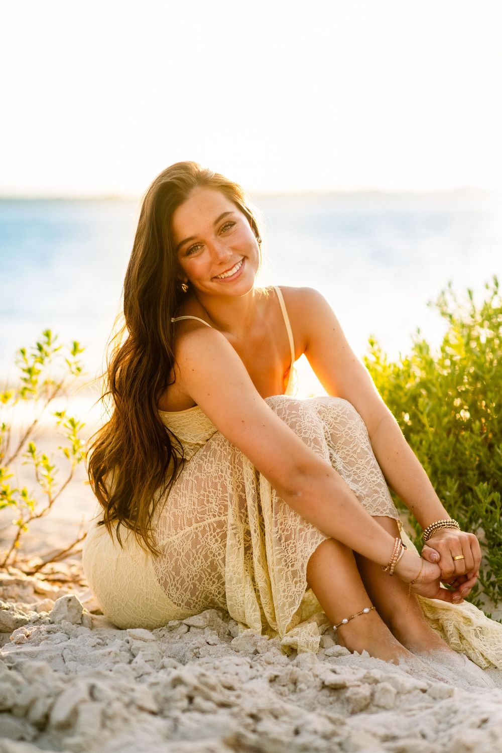 A person in a cream-colored dress sits on sandy beach during golden hour.
