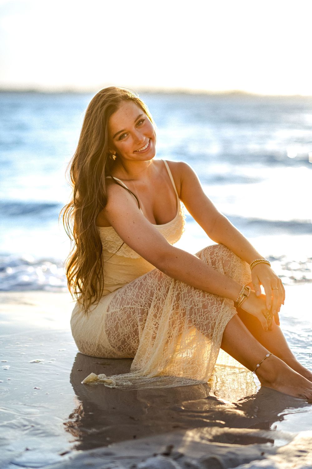 Woman sitting in wet sand as waves roll in during beach photoshoot.