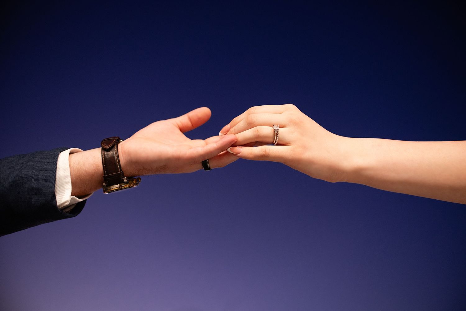 Two hands reach out towards each other in front of a dark blue background, creating a dramatic silhouette effect.