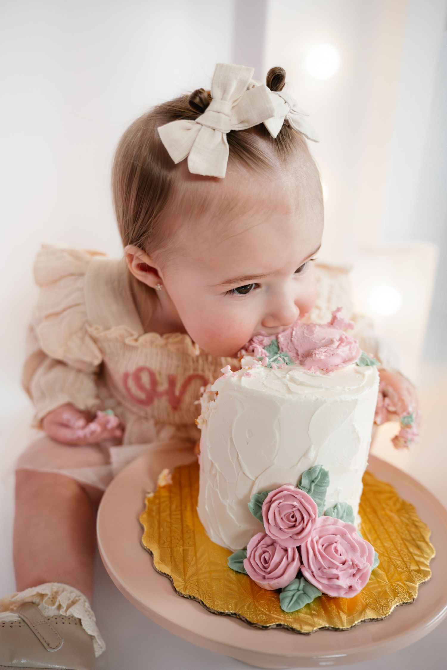 An adorable baby girl with a bow headband eats her floral first birthday smash cake.