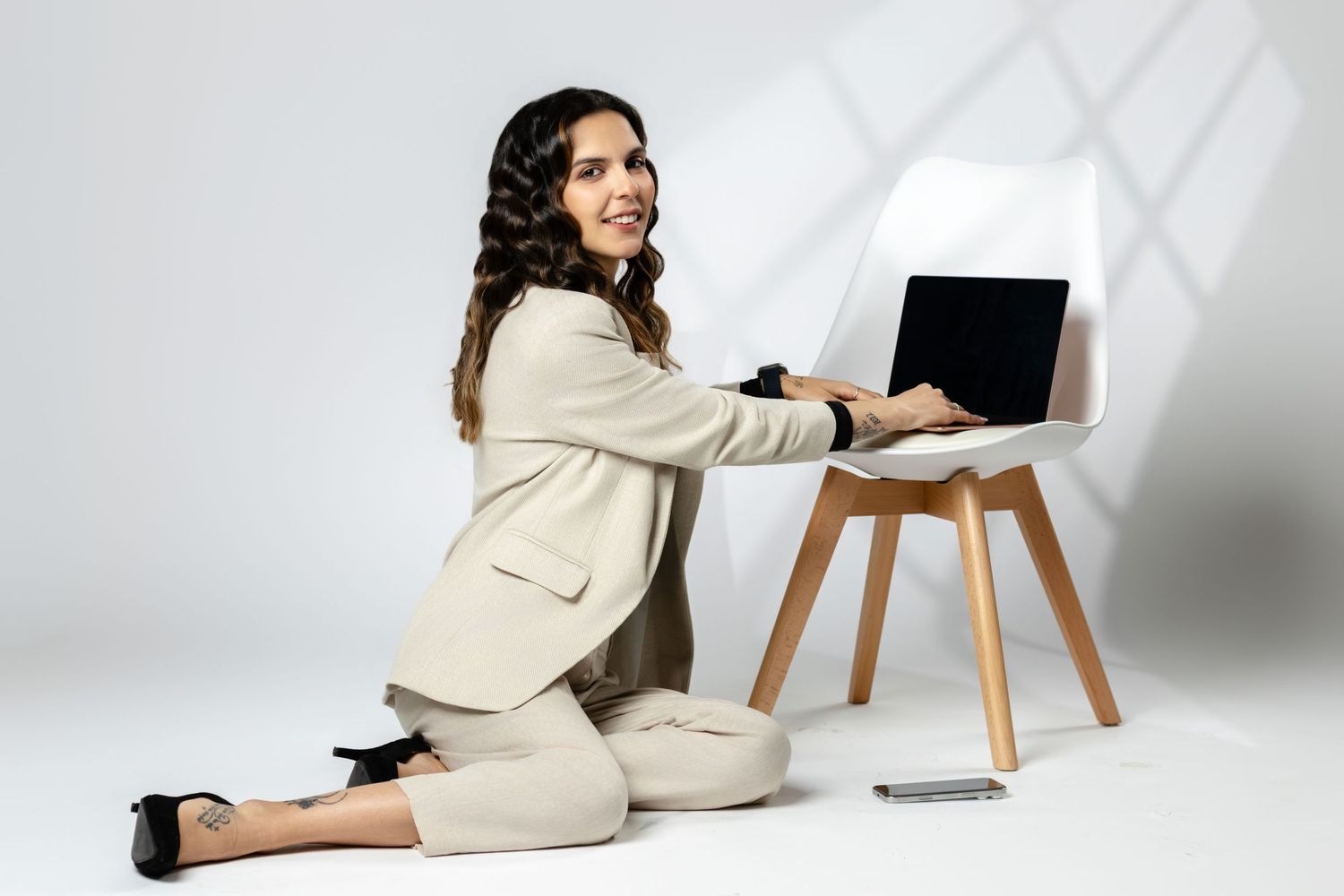 Professional workspace scene with person in light blazer working on laptop near minimalist chair.