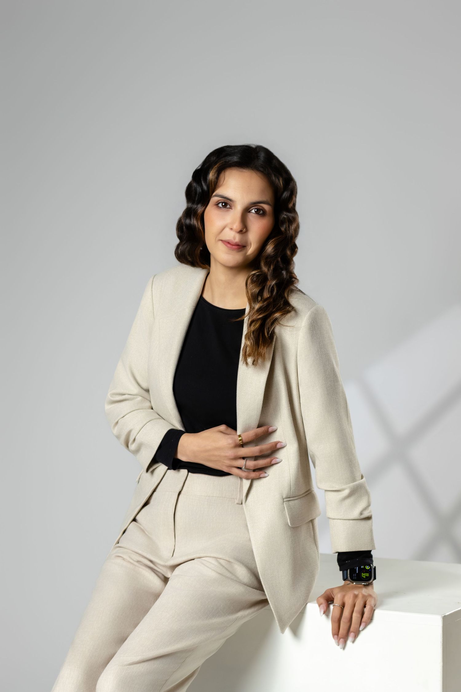 Professional portrait of model wearing cream suit and black top against grey studio background.