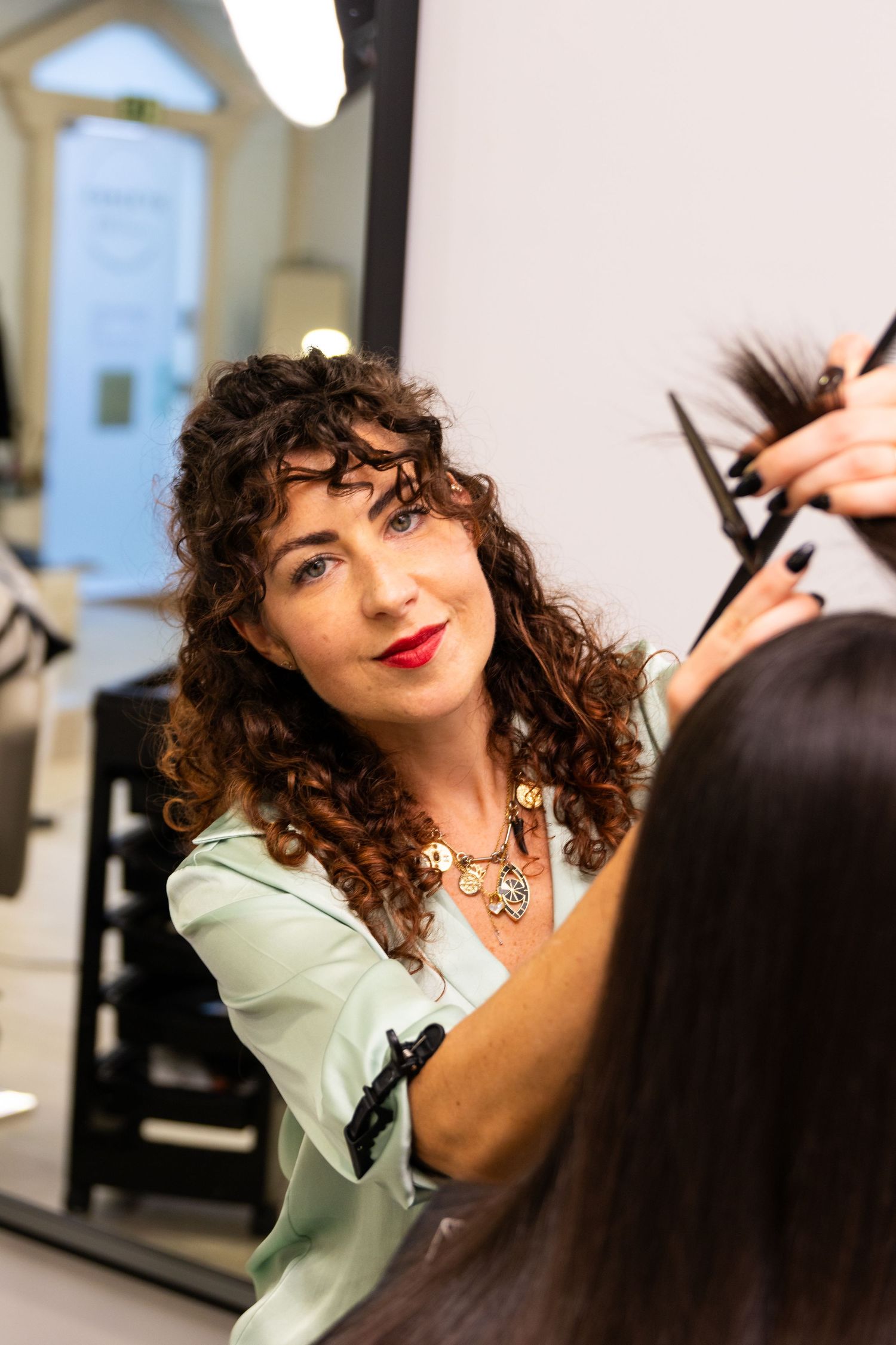 A hairstylist with curly hair works on cutting a client's hair in a salon.