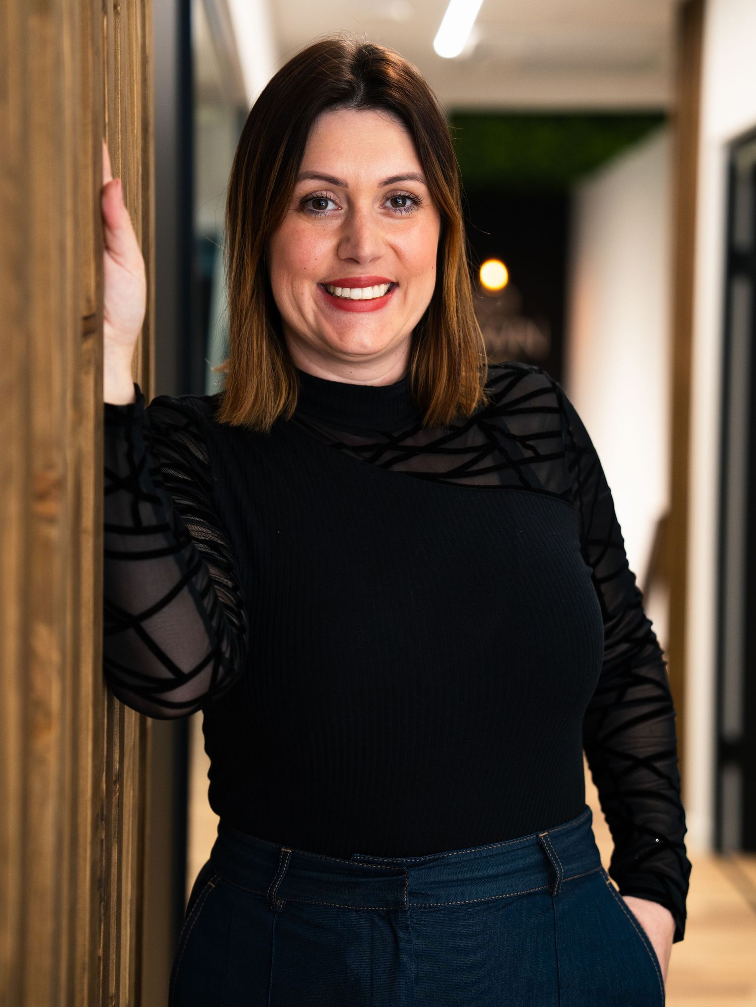 Professional in black top poses confidently in office hallway setting.
