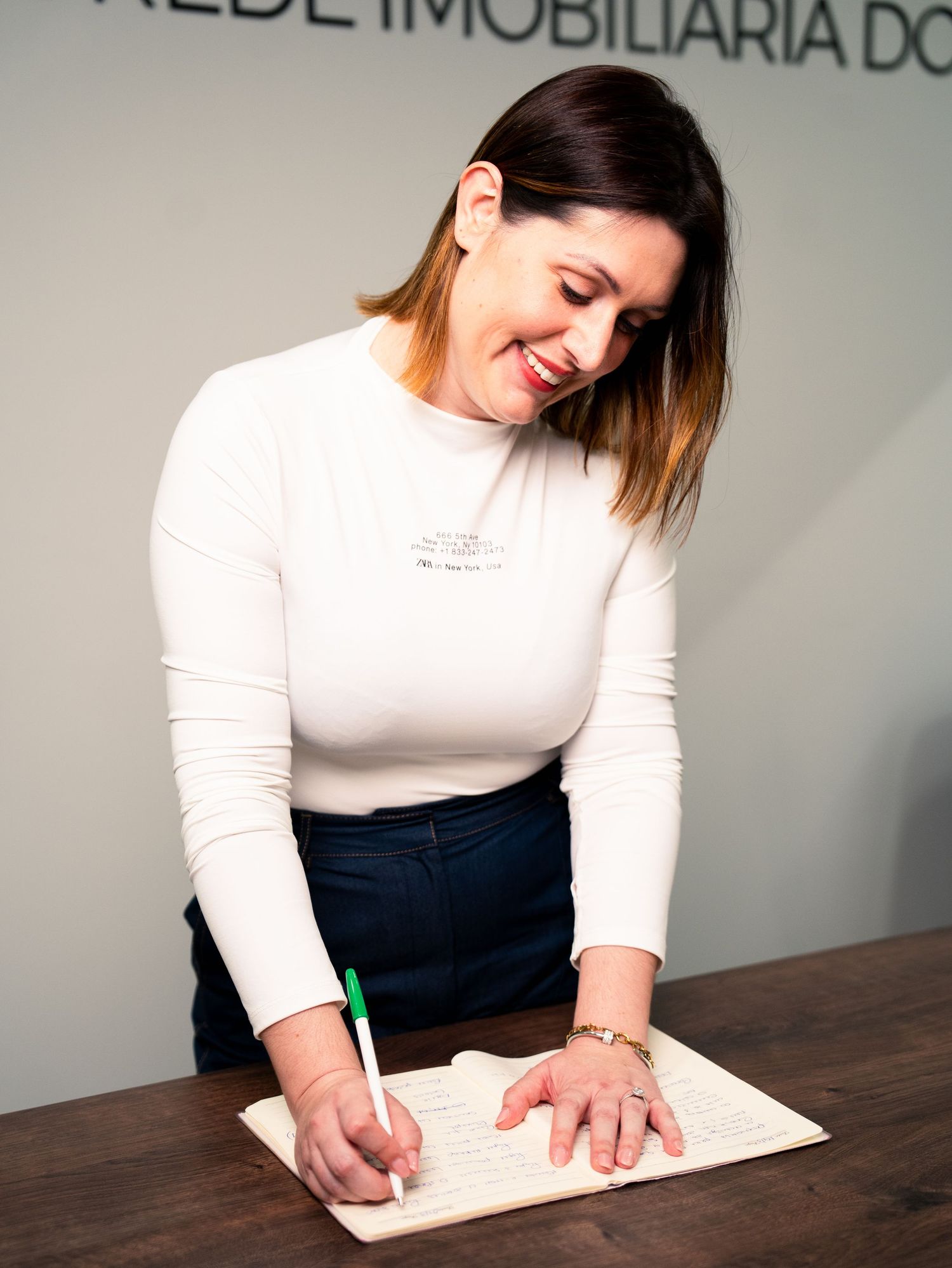 Professional signing documents at a desk while wearing a white long-sleeved top.