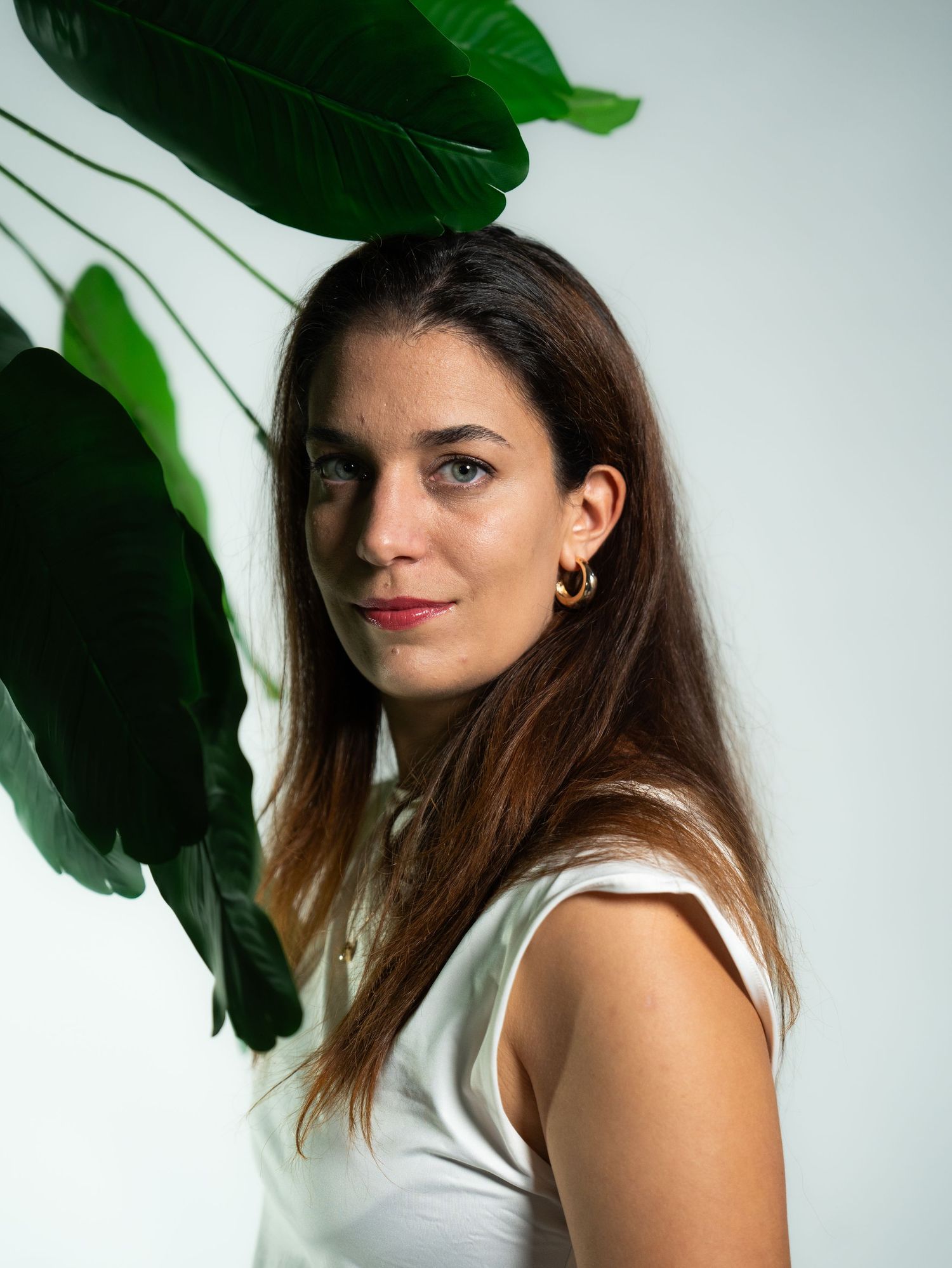 A portrait of a woman in white top against a backdrop of large green leaves.