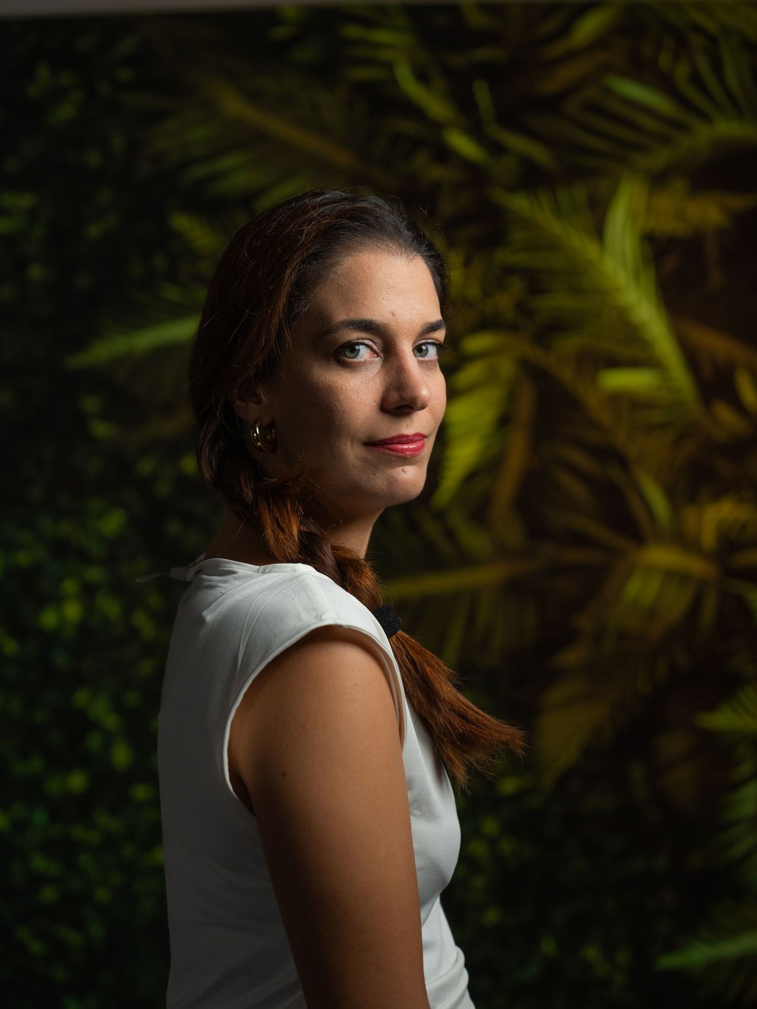 Artistic portrait in dark setting with dramatic lighting against tropical foliage background.