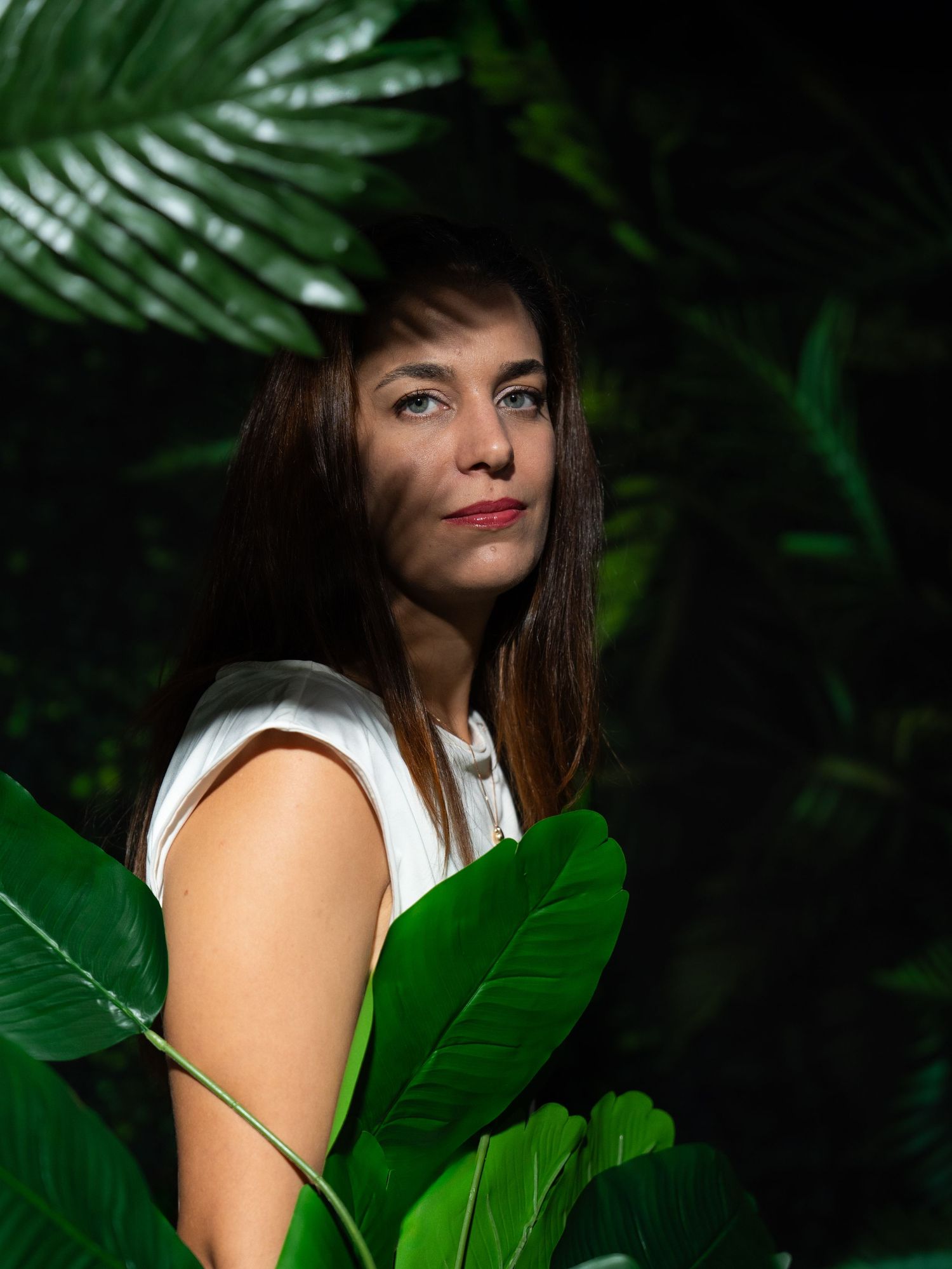 Moody portrait with green palm leaves creating natural framing in low-key lighting.