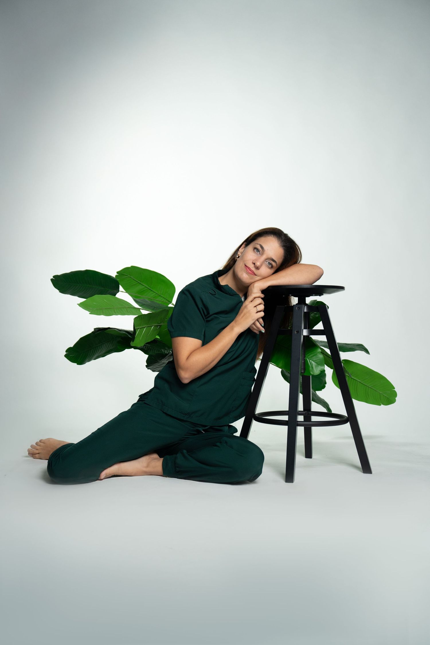Relaxed studio portrait with person reclining on black stool against white backdrop.